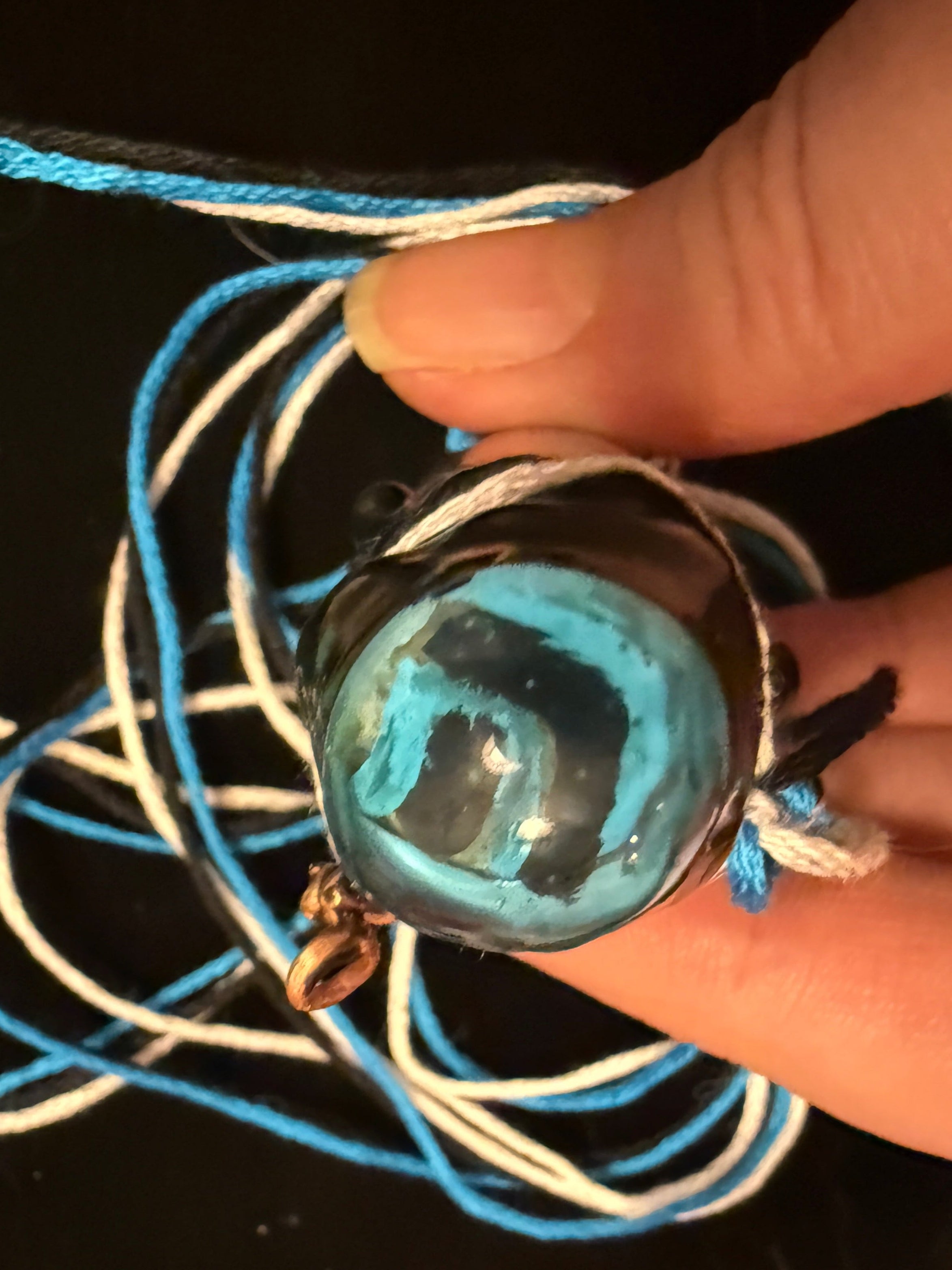 Close-up of a hand holding a blue and black pendant with a blurred background