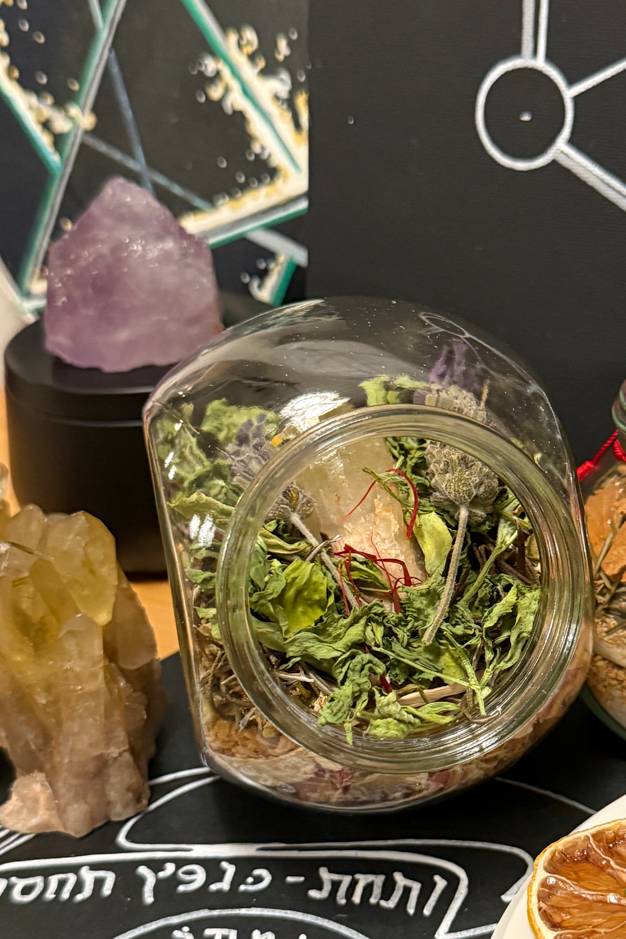 Jars with dried herbs, crystals, and a tarot card on a black surface